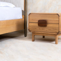 Wooden bedside table with single drawer beside a modern canopy bed