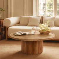 Round fluted wooden coffee table styled in a modern living room with a beige sofa and decorative accessories.