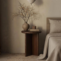 Dark brown Nashi wooden side table styled beside a bed with a decorative vase and books.